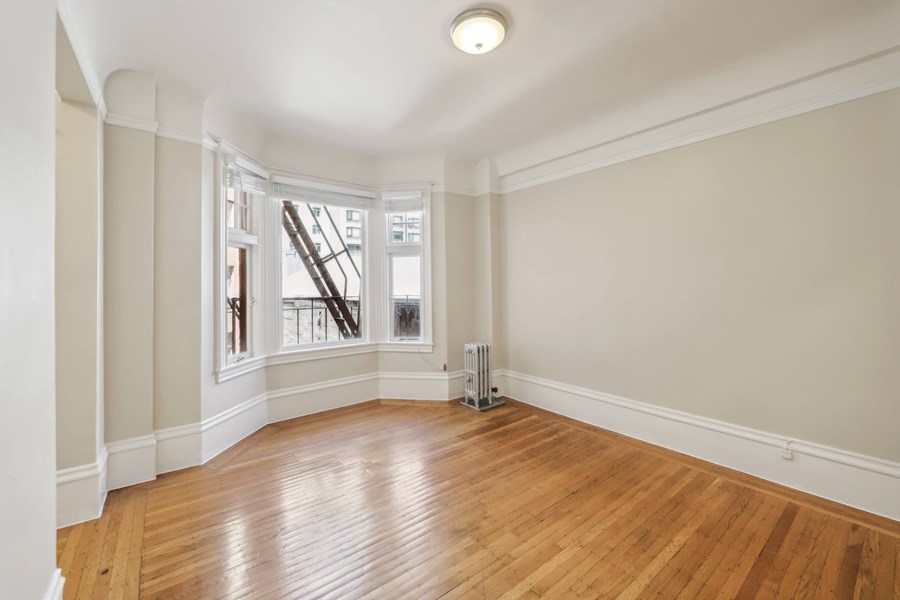 A room with wooden floors and a window with a view of a building outside.